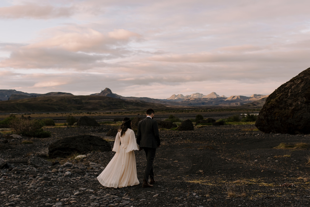 A couple walks into the sunset hand in hand surrounded by mountains lit up by the fading sun. 
