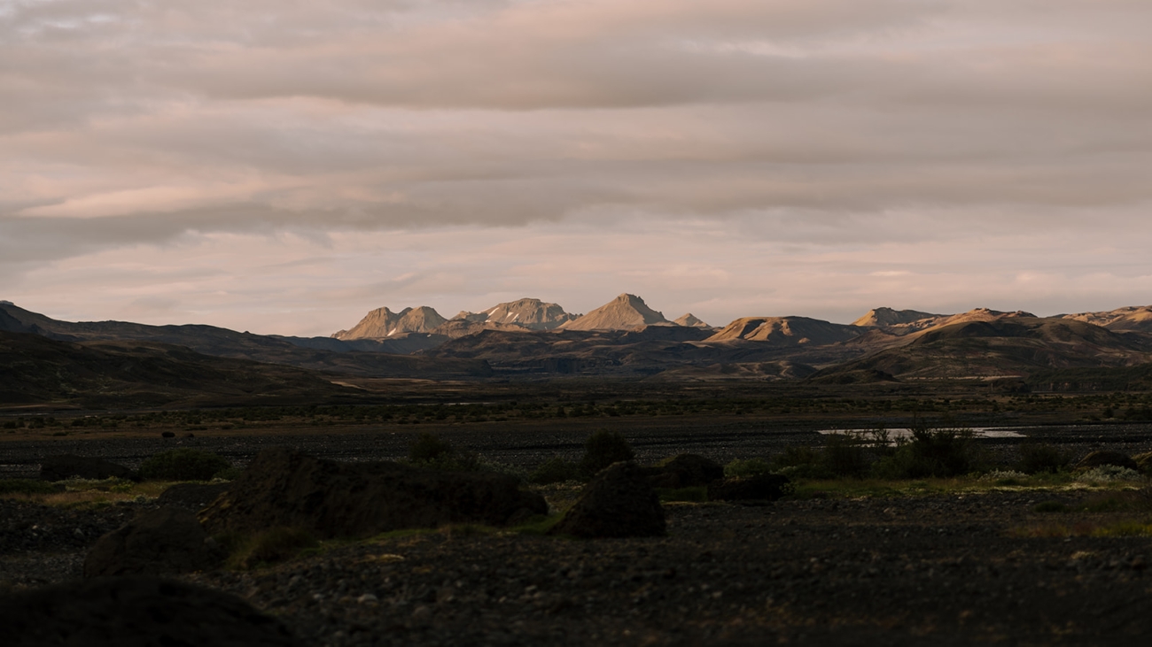 Distant mountains bathed in sunlight looming over a plain covered in shadow at dusk in Iceland. 