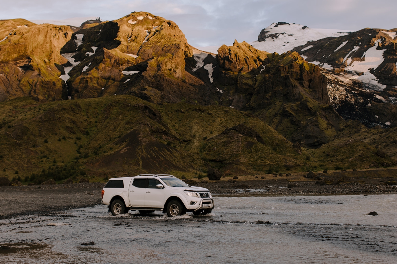 A 4x4 truck crosses one of the many rivers on the way back from Þórsmörk as the evening sun lights up the mountains in the background.