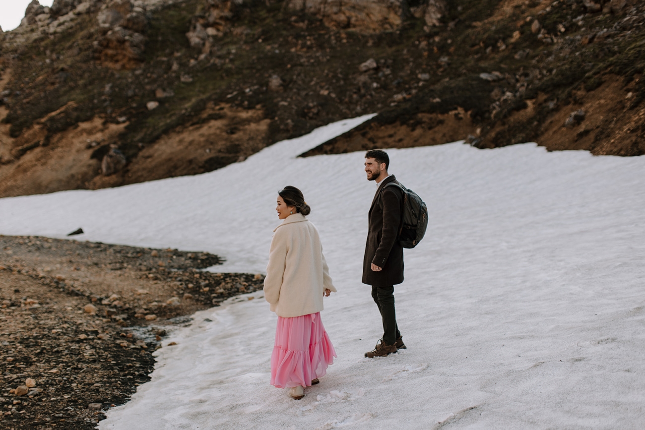 A couple takes in their surroundings while standing on a snow bank in the middle of summer in the Icelandic highlands. 