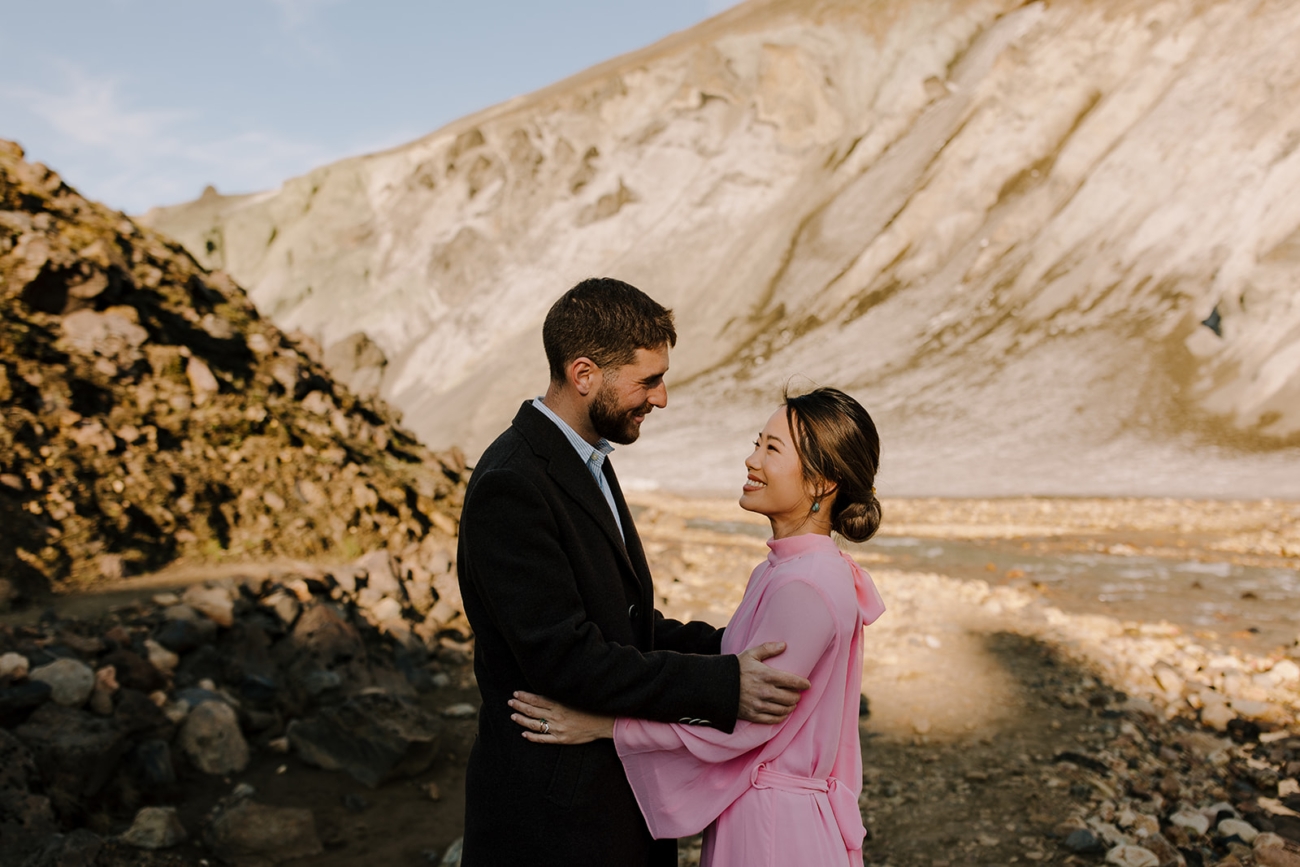 A couple looks lovingly into each other eyes with colourful Rhyolite mountains behind them lit up by the evening sun. 