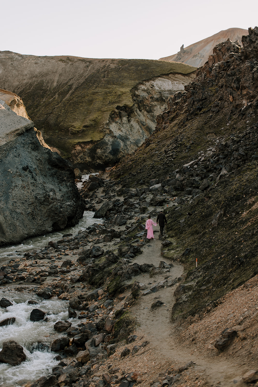 A women wearing a pink dress hikes up a geothermaly active canyon in Landmannalaugar, Iceland.