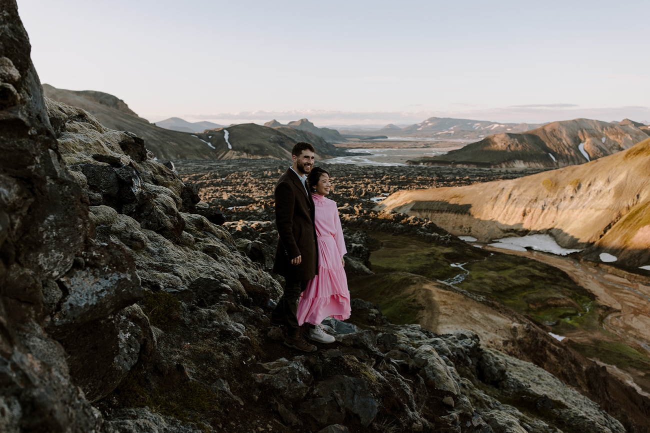 A couple standing on top of a hill looking over the vast landscapes of the highlands of Iceland.