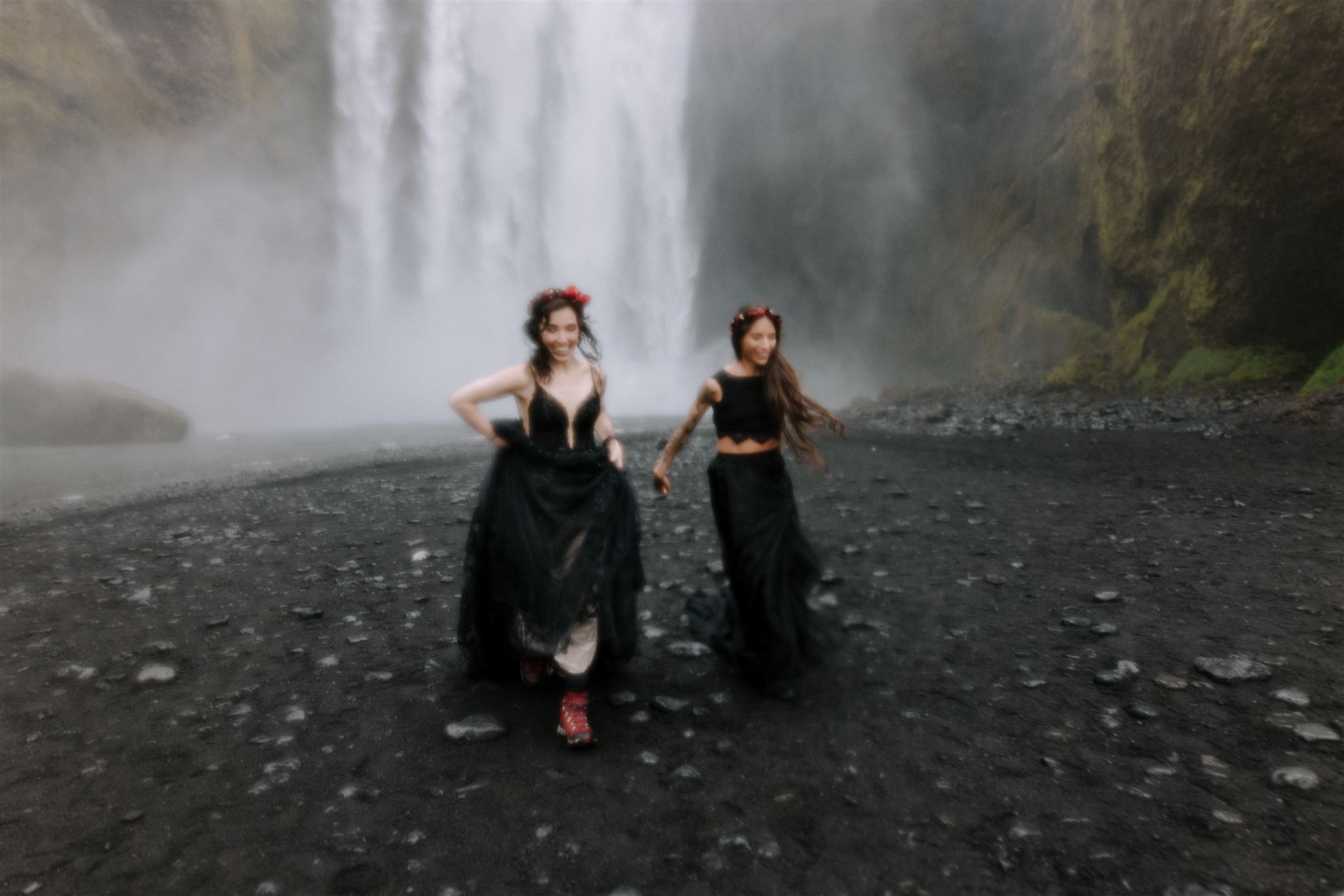 A lesbian couple running through the mists of Skógafoss waterfall in Iceland.