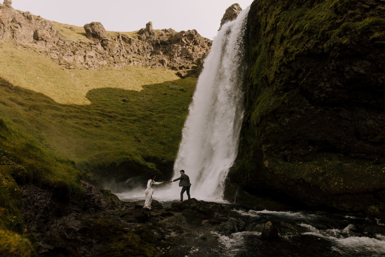 A couple hike next to a high waterfall hidden in a canyon somewhere in Iceland.